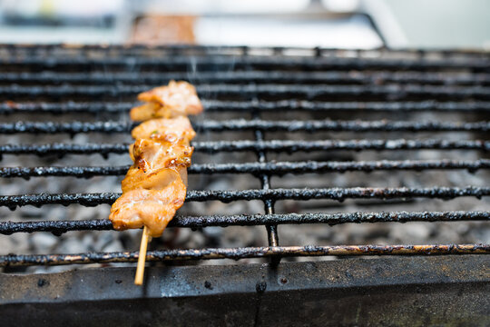 A Thai grilling pork skewers on stove