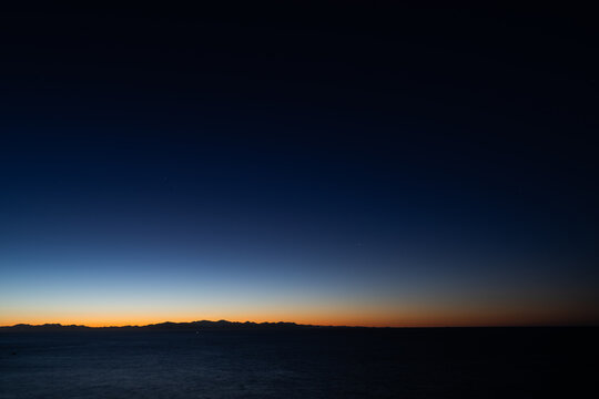Predawn horizon with orange glow over mountain range and dark sea