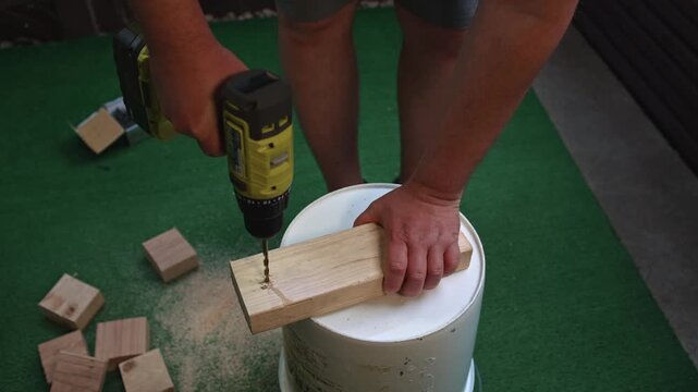 Man drilling hole in wooden board with drill holding piece by hand creating process of material processing and carpentry tasks during construction work