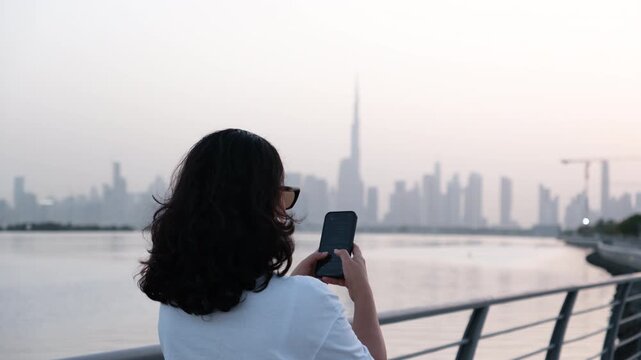 Close up woman using smartphone with Dubai skyline and Burj Khalifa in background, mobile lifestyle 4K
