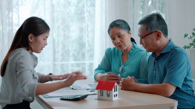 Professional financial advisor meeting with senior couple at home, discussing real estate investment, mortgage planning, and retirement finance with house model on table.
