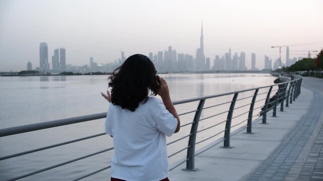 young woman on the bridge talking on phone with Dubai skyline background for Dubai lifestyle and young woman entrepreneur concept video 
