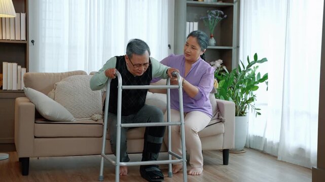 Senior man recovering mobility with walking aid supported by caregiver in home environment, emphasizing rehabilitation and elderly care.
