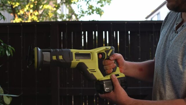 Man inserting battery into reciprocating saw and starting tool operation creating process of equipment preparation and demonstration of power tool work before construction tasks