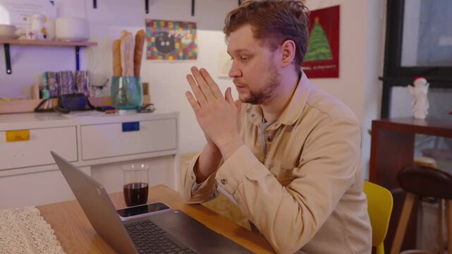 Anxious young man working from home on a laptop, feeling stressed and overwhelmed by his job, covering his face with his hands in frustration and experiencing burnout from overwork