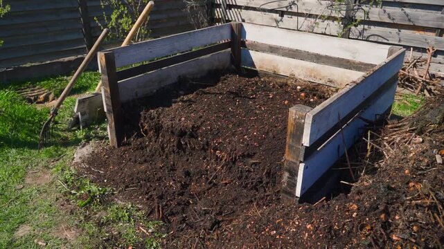 Wooden compost bin with ready vermicompost and pitchfork in spring backyard garden