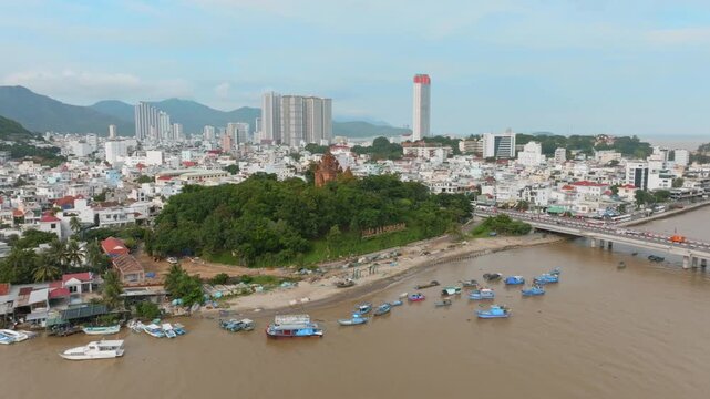 Nha Trang, Vietnam - Boats are moored along the Cai River bank, with the Ponagar Cham Towers and modern city skyline in the background.
