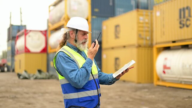 Professional logistics manager in safety gear coordinates shipping operations using a digital tablet and walkie talkie