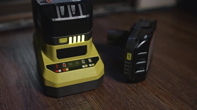 Battery charging on desktop power tool charger with indicator lights showing charging process energy monitoring and tool preparation for work in workshop environment
