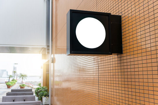 Mockup of blank white circular signage on black square light box wall mounted, Empty round store sign template on modern brown tile building exterior for branding, projection signage board mockup
