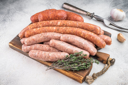 Raw sausage assortment on wooden board isolated on white background. Fresh seasoned pork meat links perfect for grilling barbecue cooking.
