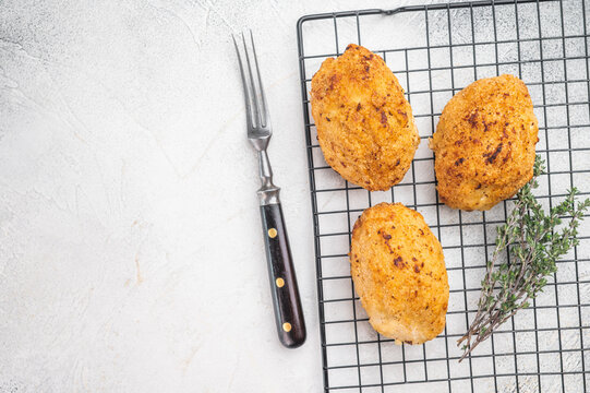 Chicken Kiev butter chicken cutlet stuffed chicken with herb butter filling on wire rack with fork on light background