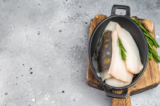 Fresh dab flatfish fillets with herbs and garlic in cast iron pan, raw seafood ingredient for healthy cooking on light textured background