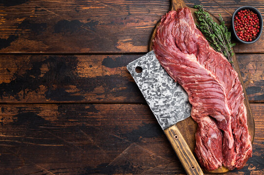 Raw beef hanger steak or onglet on wooden board with cleaver peppercorn and herbs, rustic dark wood background with copy space