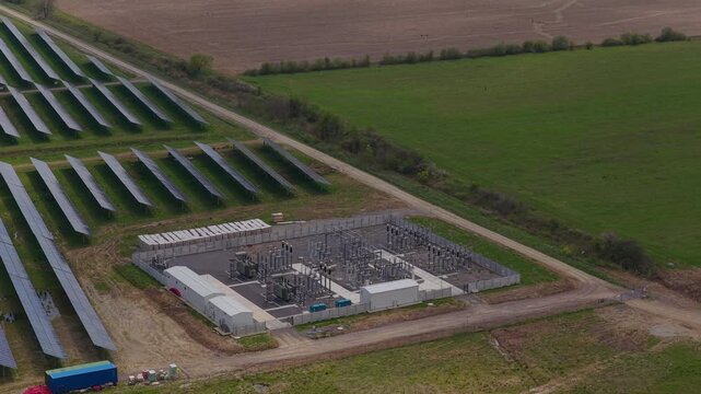 Modern transformer station and energy storage batteries at a photovoltaic power plant with clean agricultural fields providing copy space, slow orbital telephoto drone shot 4K