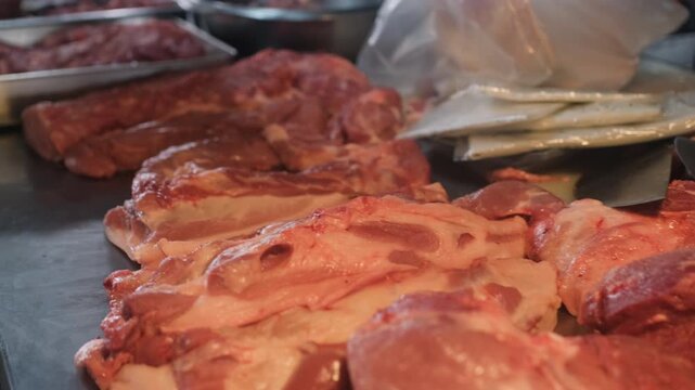 Different types of raw meat cuts displayed on butcher counter including pork and beef pieces. Fresh market selection concept