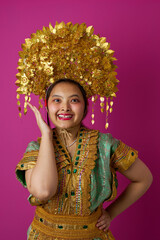 Naklejka premium Smiling Indonesian Asian Girl Wearing Ornate Gold Headdress and Traditional Costume Against Pink Background