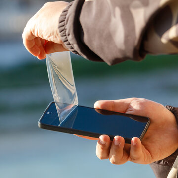 Person removing phone screen protector outdoors