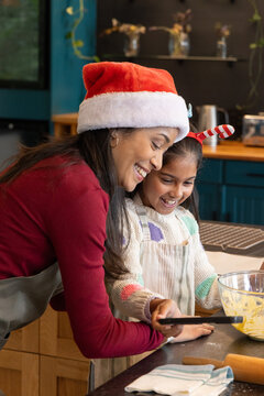 Indian mother and daughter mixing batter at home kitchen counter with Santa hat, aprons, spatula