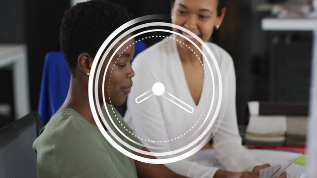 Animated clock appearing and rotating, initiating 2 women collaborating in office using PC and docs