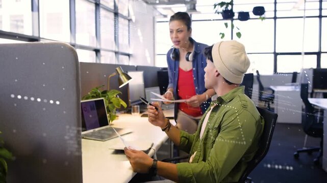Man with charts, woman walking up pointing at laptop graphs, clarifying business data, smiling