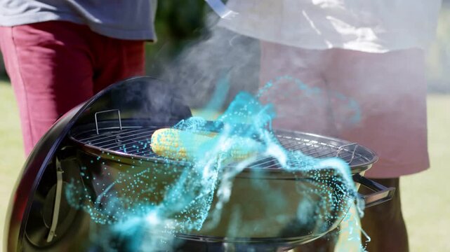 Two men tending grill lifting corn with tongs blue effect swirling over smoke helping even cooking