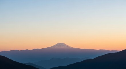 Obraz premium Majestic mountain peak emerges from layered ridges under a soft gradient sky at dawn or dusk