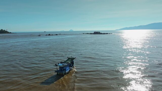A lone fishing boat sails on the calm waters near Hon da Chu, Nha Trang, Vietnam. The sun glints off the sea as the boat heads towards the shore
