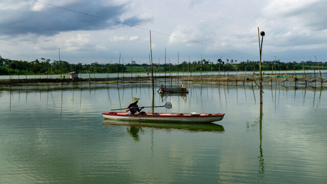A lone fisherman fishing from a small wooden boat on a calm lake, East Java.