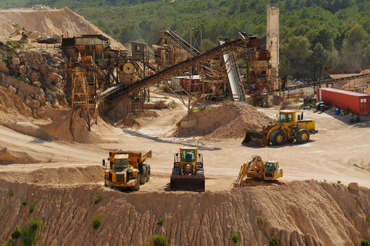 Heavy machinery working at limestone quarry with conveyor system and crushing plant in background. Industrial mining site with excavator, loader and dump truck for aggregate production.