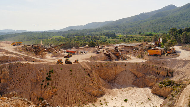 Wide view of active limestone quarry with heavy machinery, conveyor systems and processing plant surrounded by hills. Industrial mining landscape with open pit excavation and aggregate production.