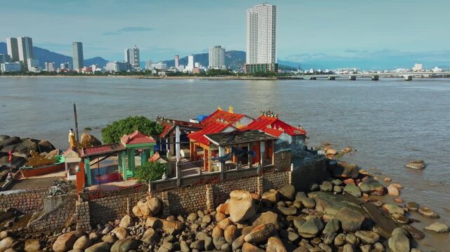 A small temple complex sits of Hon da Chu on a rocky outcrop in Nha Trang, Vietnam, with the modern city skyline in the background.