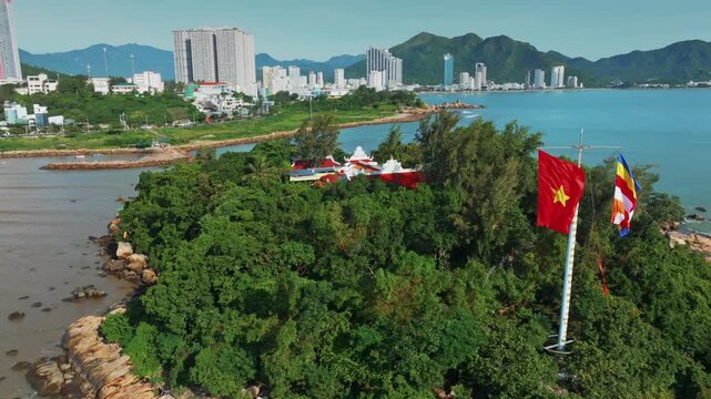 Vietnam's national flag and Buddhist flag fly on a lush green island of Chua Tu Ton overlooking the city of Nha Trang, Vietnam. The flags symbolize national pride and spiritual heritage