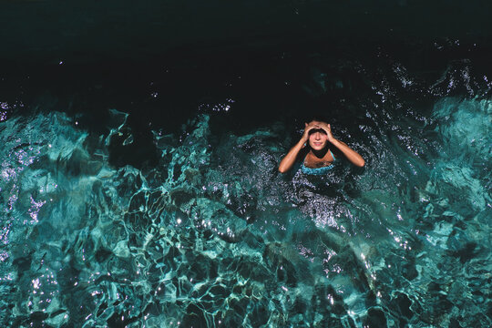 Woman holding head in wonder while floating in pool, Uluwatu, Bali