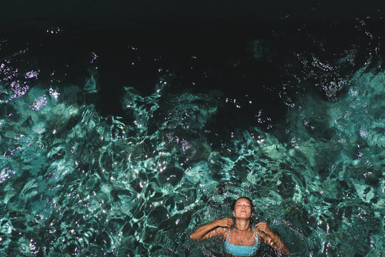 Serene woman floating on back in sparkling villa pool, Uluwatu, Bali