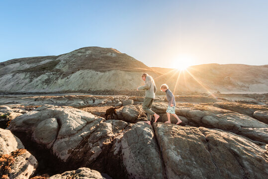 Barefoot siblings and dog walking on coastal rocks