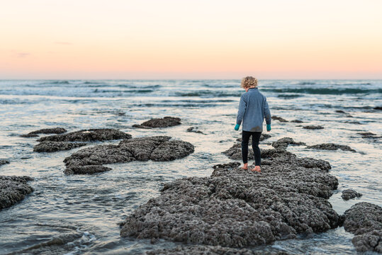 Curly haired child walking on beach rocks at sunset