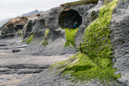Child exploring coastal cave with green algae