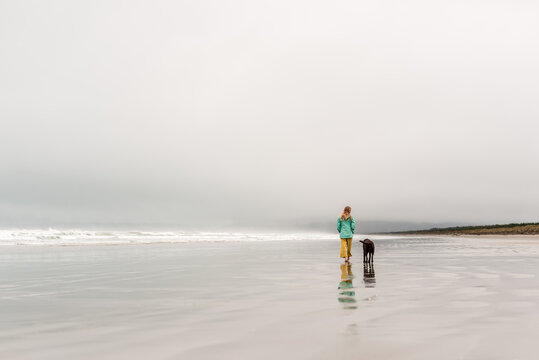 Girl and dog walking on deserted foggy beach