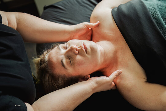 Woman receiving neck and shoulder massage, eyes closed, warm light