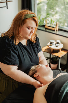 Therapist performing neck massage, hot stones tray visible in back