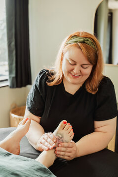 Smiling therapist giving foot massage, client's red painted toenails