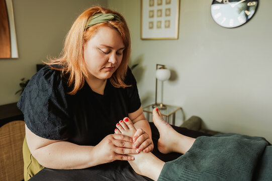 Therapist focused on foot reflexology, styled room with gold lamp