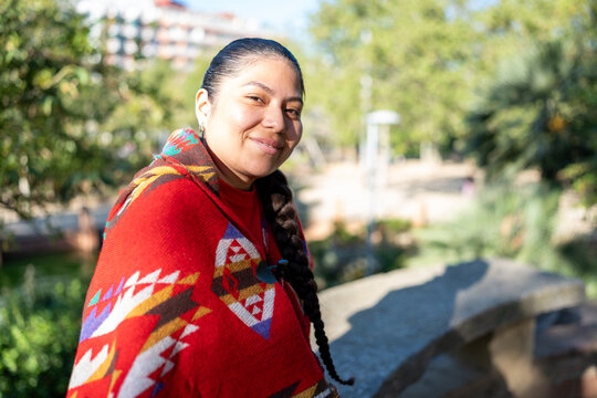 Peruvian indigenous woman smiling, wearing a traditional poncho in a sunny park