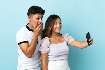 Naklejka premium Young caucasian couple isolated on blue background making a selfie with the mobile