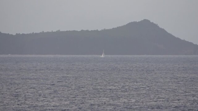 Einsames Segelboot auf dem offenen Meer vor einer fernen Insel