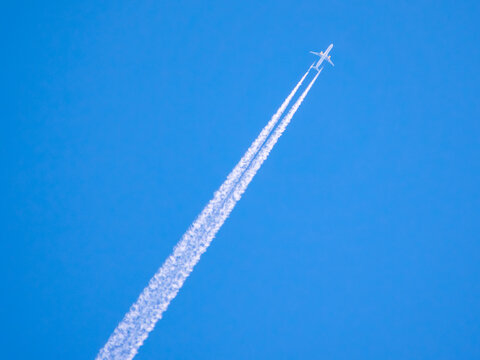 Airplane flying high in the sky leaving white trails during clear day with blue background