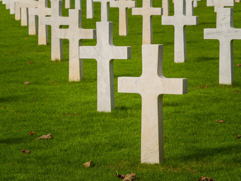 Graves with white crosses arranged in rows on green grass in a memorial cemetery during daylight hours