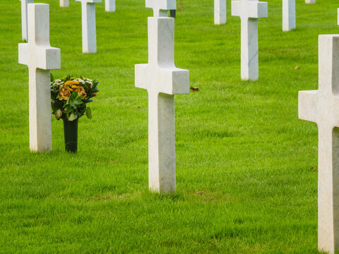 Crosses stand in a row as flowers sit at a grave in a cemetery where people remember their loved ones