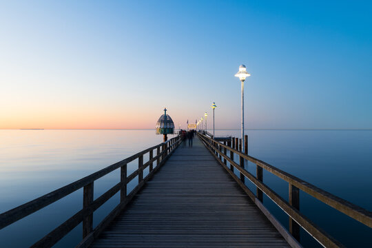 Seebr&uuml;cke Zinnowitz bei Sonnenuntergang mit Holzsteg, Lampen und ruhiger Ostsee unter klarem Himmel in der Abendd&auml;mmerung